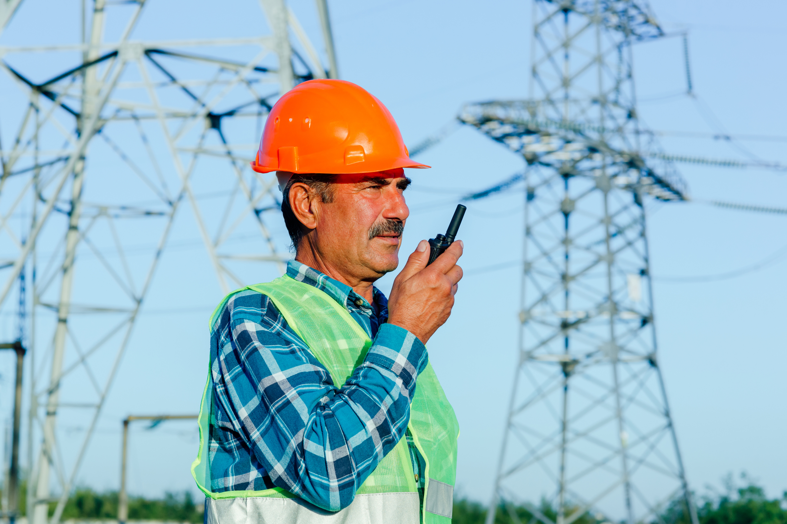 Low angle of professional electrician technician in hardhat and waistcoat speaking on portable radio Low angle of professional electrician technician in hardhat and waistcoat speaking on portable radio